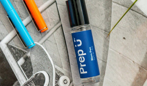 A blue Prep U balm pen on a textured background with colorful pens beside it.