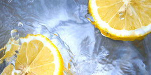Fresh lemon slices splashing in clear water, illustrating the natural essence of essential oils.