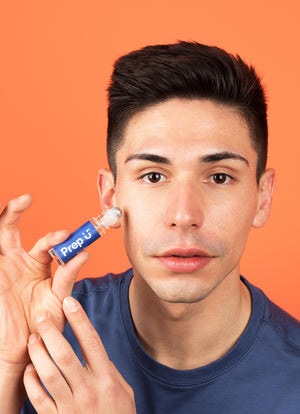 Young man holding Prep U blem pen skincare product, showcasing its application on his face against an orange background.
