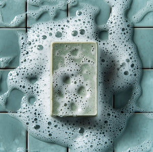 A bar of soap surrounded by bubbles on aqua tiles, creating a fresh and clean aesthetic.