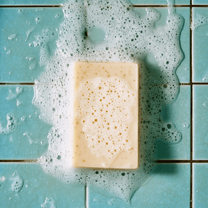 Peppermint + Oats cleansing soap bar with bubbles on blue tiles, showcasing a refreshing skincare experience.