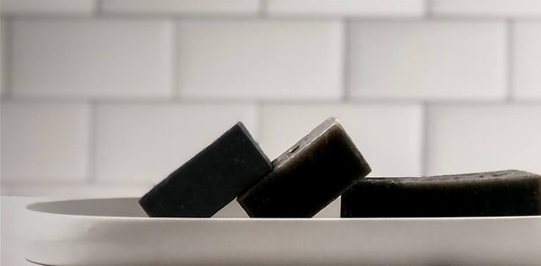 Three elegant black soap bars neatly arranged in a white dish against a classic tiled background.