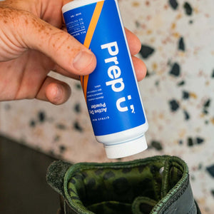 Person using Prep U Active Dry Powder to freshen up their boots, preventing moisture and odor during workouts.