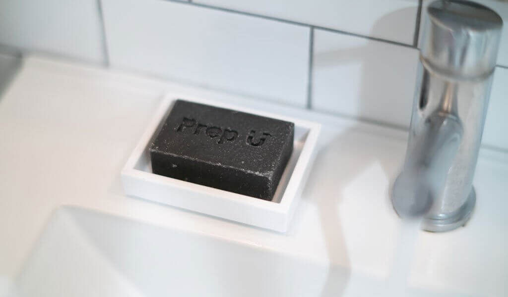 Prep U Charcoal Bar soap on white dish next to modern faucet, highlighting personal hygiene choices.