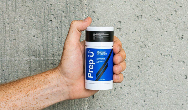 Hand holding Prep U charcoal deodorant against a concrete wall, showcasing modern odor-fighting solutions.