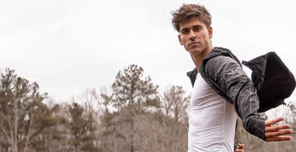 A young man in a sporty outfit poses outdoors, showcasing confidence and style against a natural backdrop.