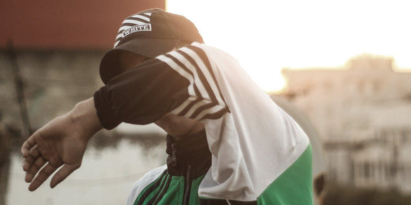 Young boy in a sporty outfit shielding his face from the sun, wearing a cap and a stylish jacket.