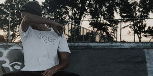 Skateboarder in a beanie wearing a white t-shirt, sitting at a skate park during sunset.