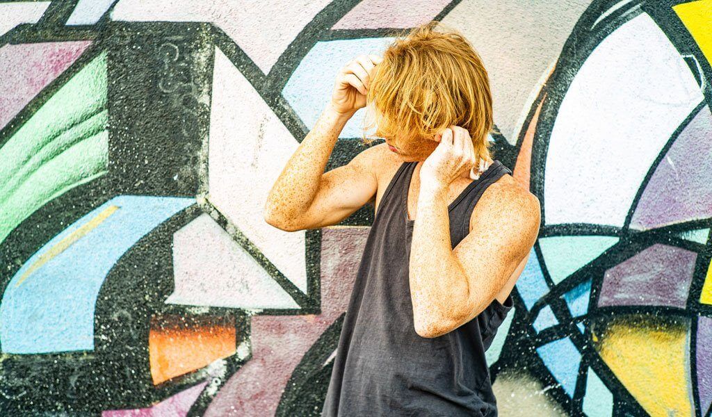Young man adjusting his hair in front of a colorful graffiti mural, showcasing urban style and carefree attitude.