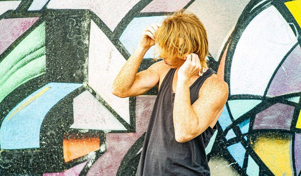 Young man adjusting his hair in front of a colorful graffiti mural, showcasing urban style and carefree attitude.