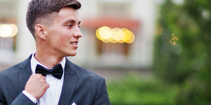 Stylish teen in a suit and bow tie ready for prom, smiling with confidence against a blurred background.