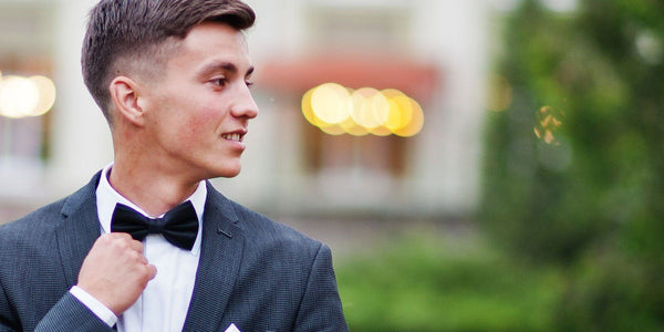 Stylish teen in a suit and bow tie ready for prom, smiling with confidence against a blurred background.