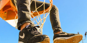 Close-up of a person's feet in black Nike sneakers resting on a basketball hoop against a clear blue sky.