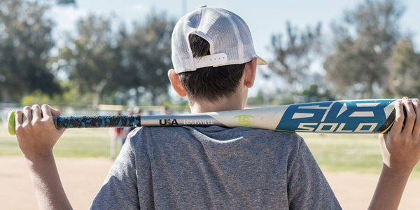 Young baseball player holding a bat over his shoulders, preparing for practice on a sunny field.