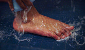 Washing a foot under running water, emphasizing cleanliness and foot care for odor control.