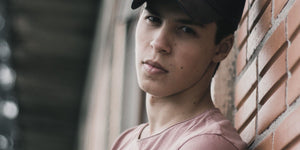 Teenage boy leaning against a brick wall, showcasing a casual look and modern hairstyle.