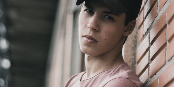 Teenage boy leaning against a brick wall, showcasing a casual look and modern hairstyle.