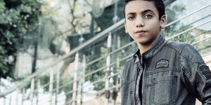A young boy in a stylish jacket stands confidently in an outdoor setting.