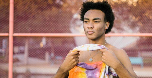 Young man with curly hair holding a colorful tie-dye towel, looking contemplative outdoors.