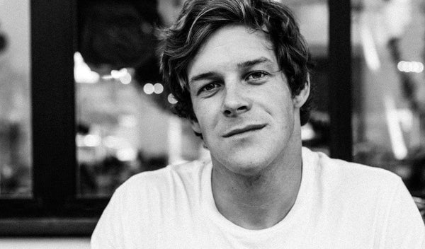 Smiling young man in a casual white t-shirt, captured in a candid black and white photograph.