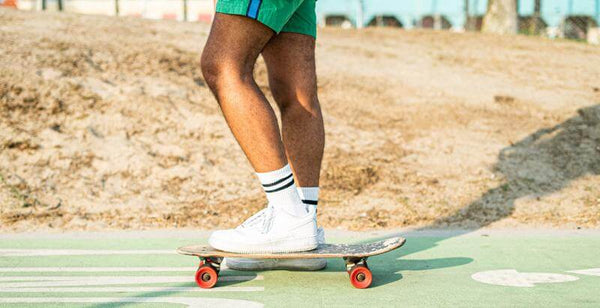 Close-up of a person skateboarding in stylish shorts and sneakers on a sunny day.