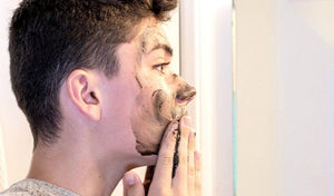 Teen applying a clay mask on their face while looking in the mirror, preparing for back-to-school skincare.