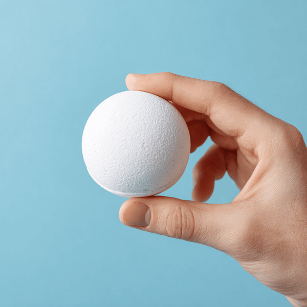 Person holding a white muscle bath bomb against a light blue background, promoting relaxation and recovery.