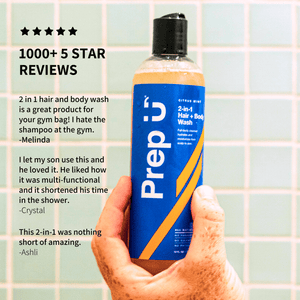 Hand holding a bottle of Prep U 2-in-1 hair and body wash with customer reviews on a tiled bathroom wall background.